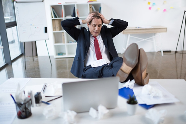 Stressed mature businessman sitting at table with laptop and ges Stressed mature businessman sitting at table with laptop and ges